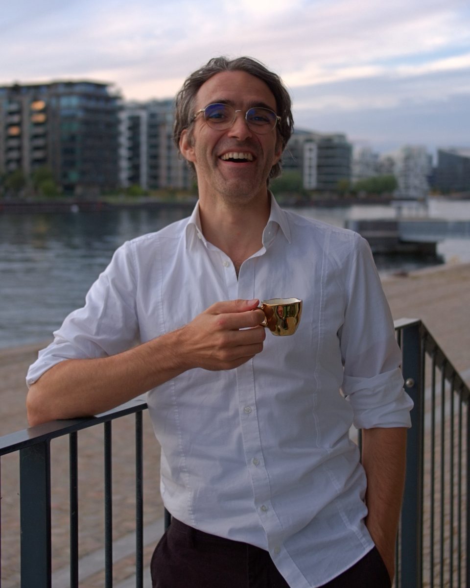 Prof. Dr. Nicco Krezdorn laughing with an espresso cup by the water in Copenhagen